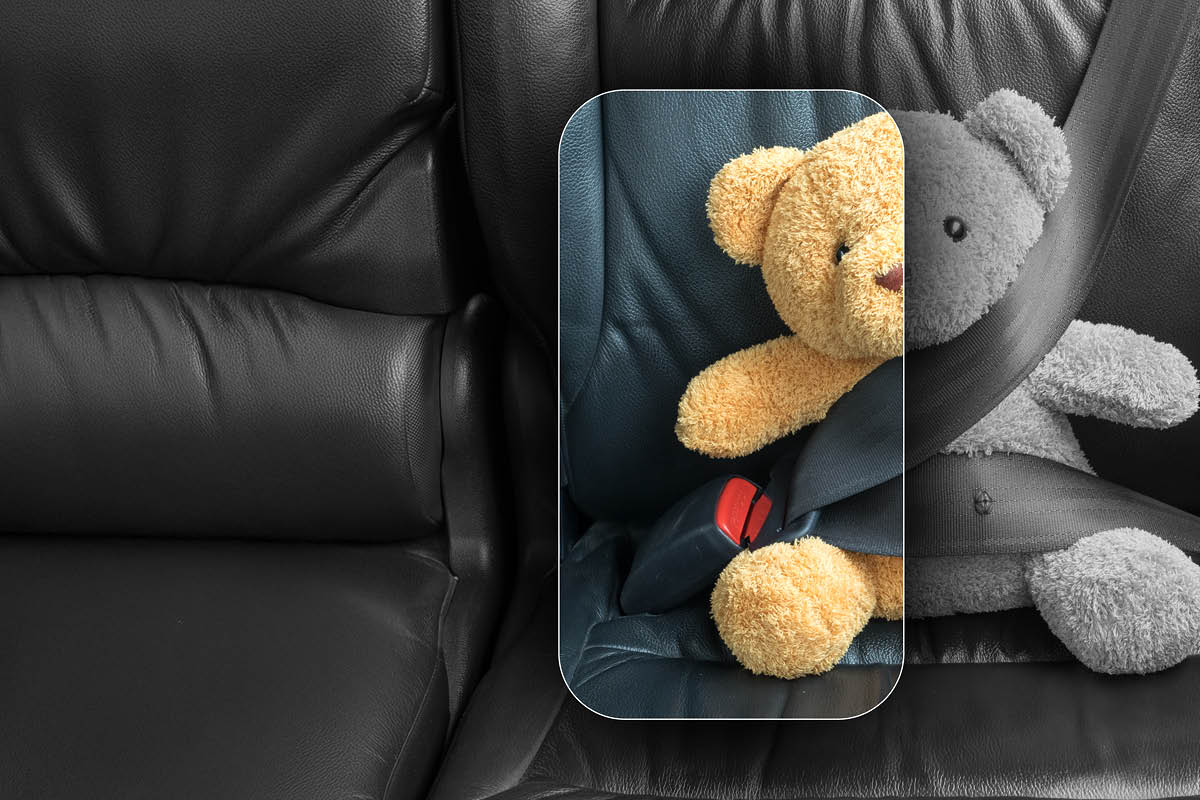 Ein Stoffteddy sitzt angeschnallt auf einem schwarzen Ledersitz, wobei der Anschnallgurt Sicherheit symbolisiert und der farbige Ausschnitt das Motiv hervorhebt.